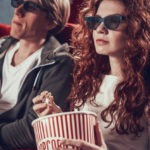 Young couple with 3d glasses eats popcorn and sitting in cinema.