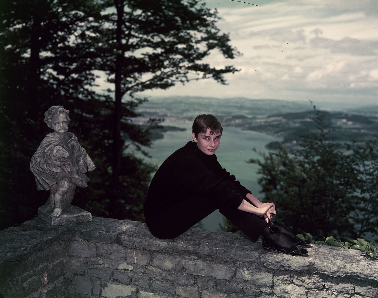 a-short-haired-Audrey-Hepburn-wearing-her-signature-all-black-look-sitting-on-a-ledge